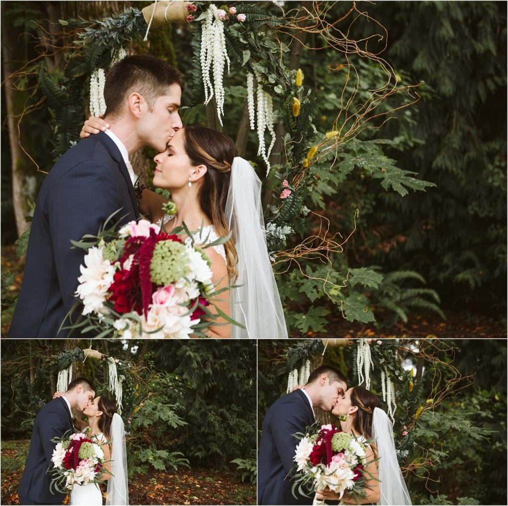 Premier snohomish & seattle wedding photographer | gsquared weddings photography a bride and groom stand under a floral arch in an outdoor snohomish setting The groom kisses the brides forehead as she holds a bouquet both dressed in wedding attire surrounded by lush greenery Perfect for a seattle wedding engagement | serving snohomish seattle                   & beyond