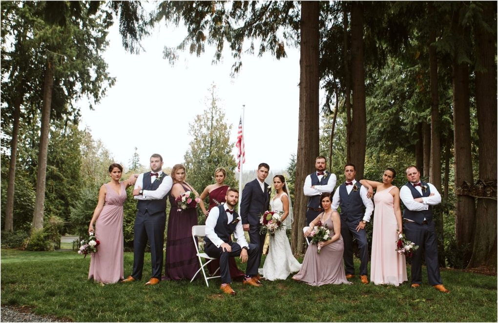 Premier snohomish & seattle wedding photographer | gsquared weddings photography a wedding party poses outdoors among tall trees in snohomish The bride and groom stand in the center surrounded by bridesmaids in mauve dresses and groomsmen in dark vests and bow ties An american flag is visible in the background | serving snohomish seattle                   & beyond