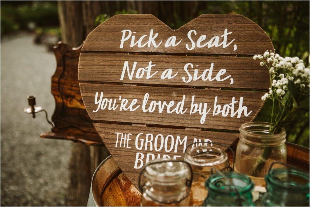 Premier snohomish & seattle wedding photographer | gsquared weddings photography a wooden heart shaped sign reads pick a seat not a side youre loved by both the groom and bride surrounded by flowers and glass jars at a charming snohomish seattle wedding venue | serving snohomish seattle                   & beyond