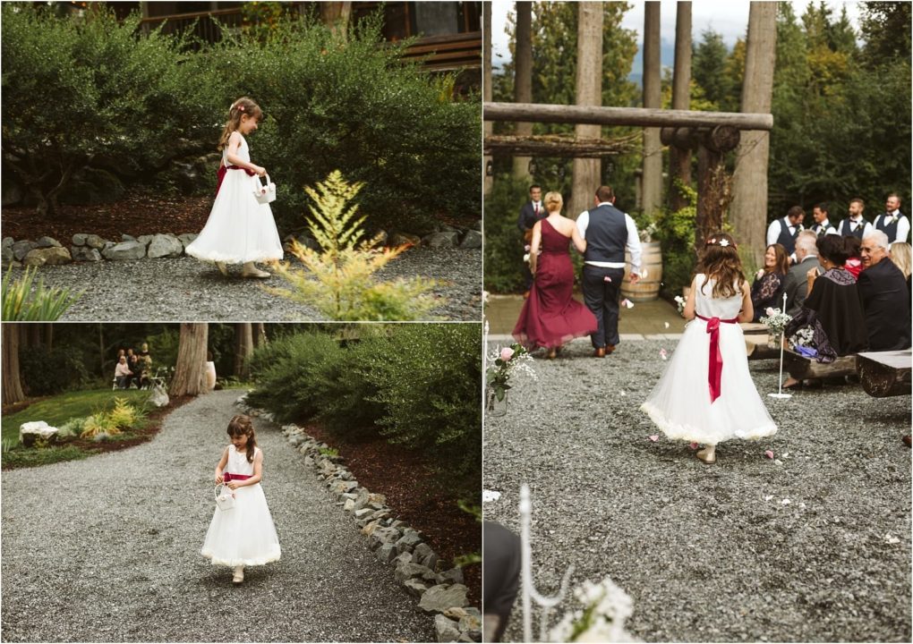 Premier snohomish & seattle wedding photographer | gsquared weddings photography a young flower girl in a white dress with a red sash walks along a gravel path at an outdoor snohomish wedding surrounded by greenery and guests seated nearby | serving snohomish seattle                   & beyond