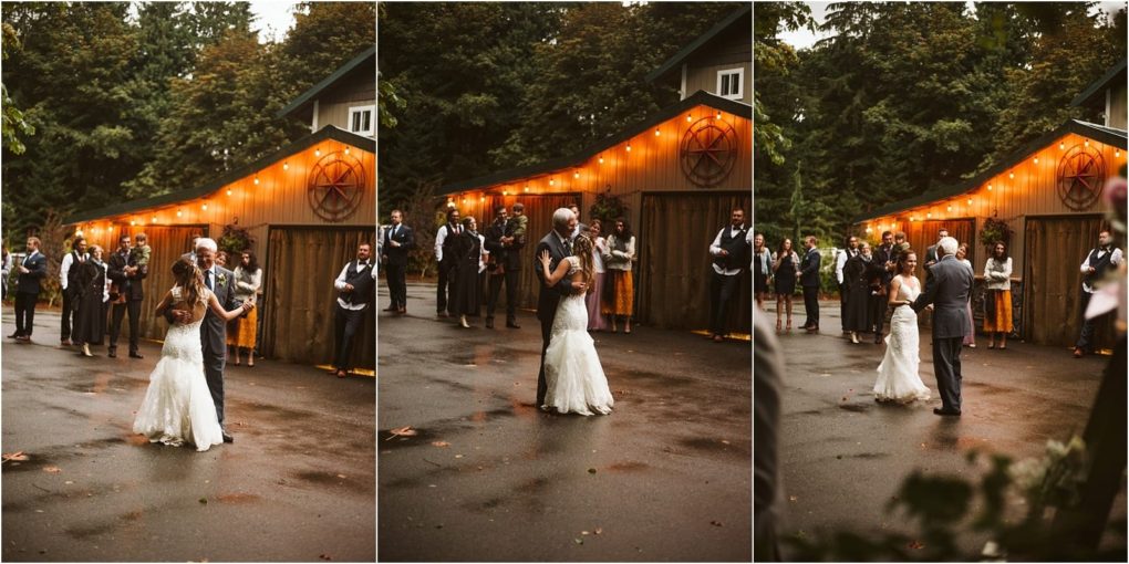 Premier snohomish & seattle wedding photographer | gsquared weddings photography a bride in a white gown dances with her father outdoors on a rainy snohomish day while wedding guests watch in front of a warmly lit rustic barn surrounded by trees | serving snohomish seattle                   & beyond