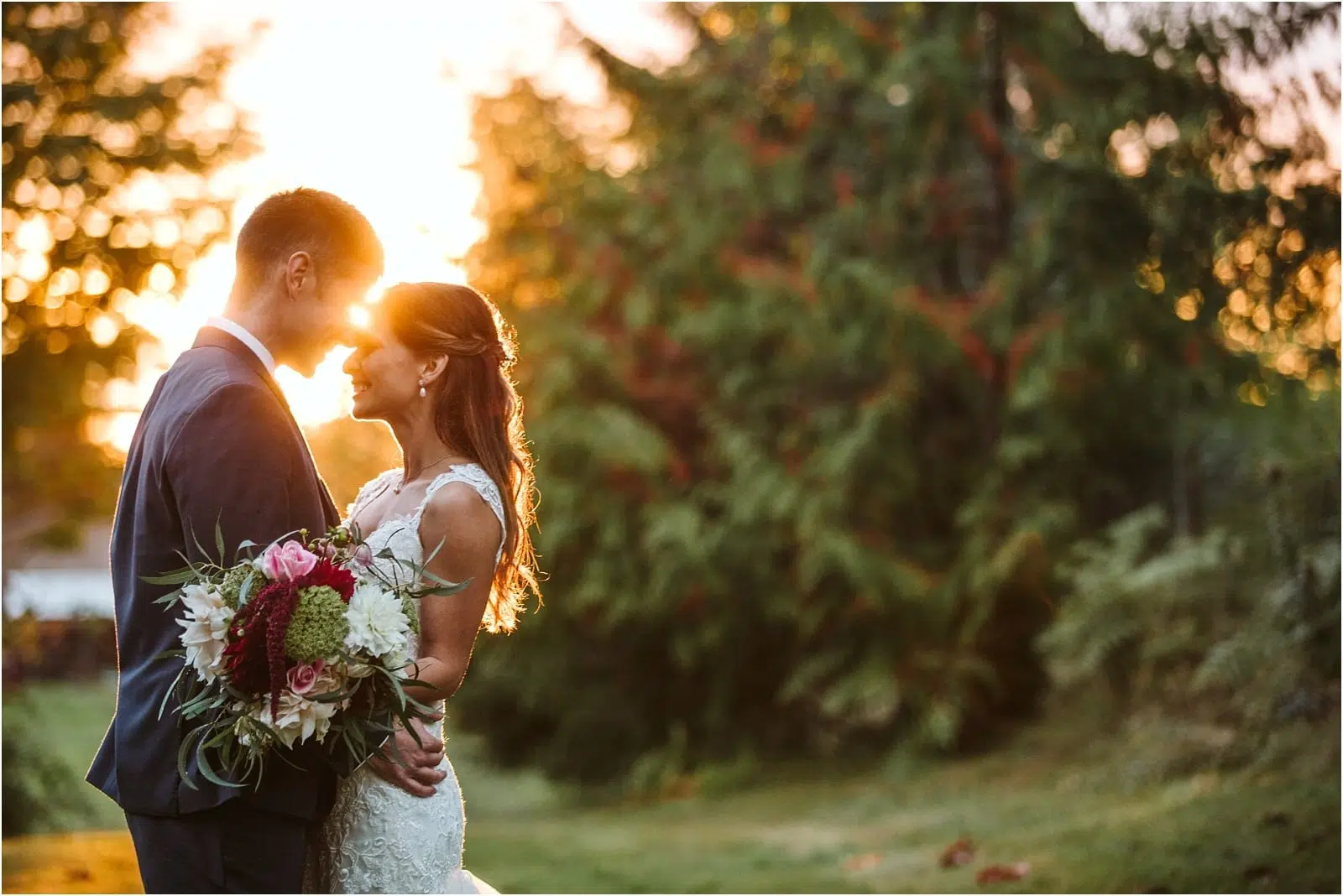 Premier Snohomish & Seattle Wedding Photographer | GSquared Weddings Photography A bride and groom stand close together outdoors at sunset, smiling and holding a bouquet of flowers, with soft sunlight filtering through trees in the background—a perfect Snohomish Seattle wedding moment. 47.9129° N, 122.0982° W | Serving Snohomish, Seattle , Orlando & Beyond