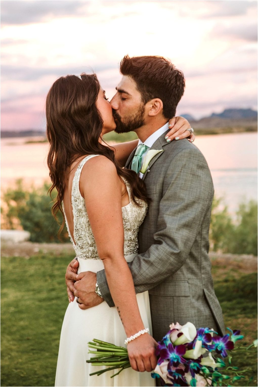 Premier snohomish & seattle wedding photographer | gsquared weddings photography a bride and groom share a romantic kiss outdoors at sunset by a lake near snohomish The bride holds a bouquet and the groom wears a gray suit and mint green tie perfect for their dreamy seattle wedding The sky is colorful with soft clouds | serving snohomish seattle                   & beyond