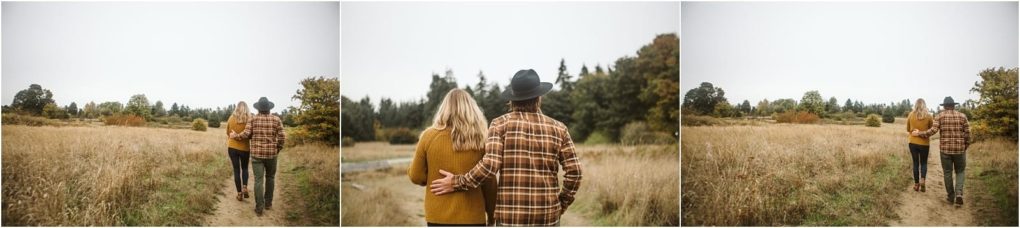 Premier snohomish & seattle wedding photographer | gsquared weddings photography a couple walks together through a grassy field on a cloudy day near snohomish with autumn trees around thema perfect seattle wedding engagement moment The woman wears a mustard sweater and the man sports a plaid shirt and hat | serving snohomish seattle                   & beyond