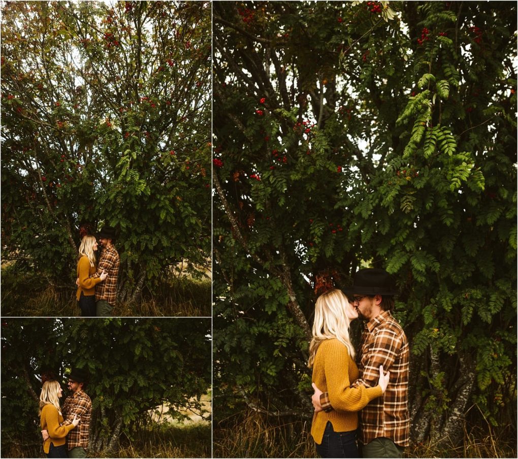 Premier snohomish & seattle wedding photographer | gsquared weddings photography a couple stands close together under a large tree with green leaves and red berries sharing a quiet intimate moment Capturing the warmth of a snohomish engagement the woman in a mustard sweater faces her partner in plaid and hat | serving snohomish seattle                   & beyond