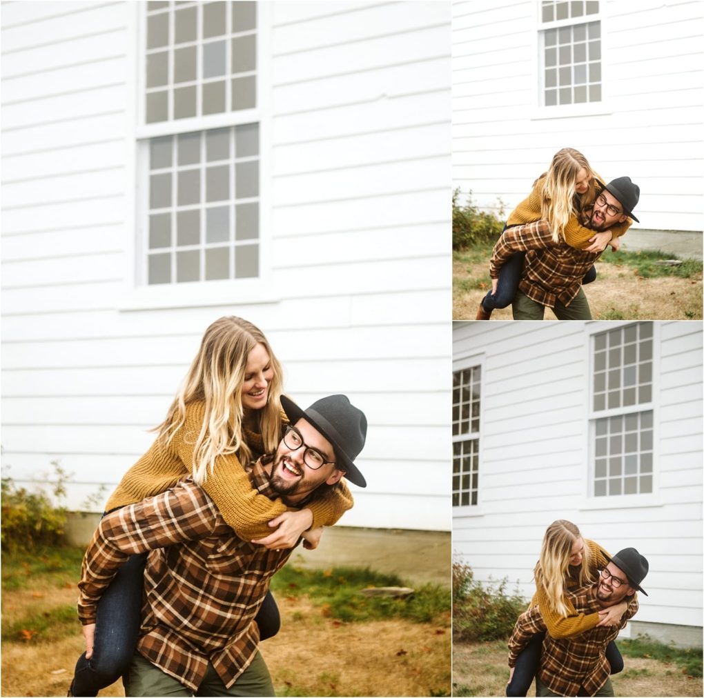 Premier snohomish & seattle wedding photographer | gsquared weddings photography a man in a plaid shirt and hat gives a piggyback ride to a smiling woman in a mustard sweater in front of a white building with large windows they laugh and play together outdoors during their snohomish seattle engagement | serving snohomish seattle                   & beyond