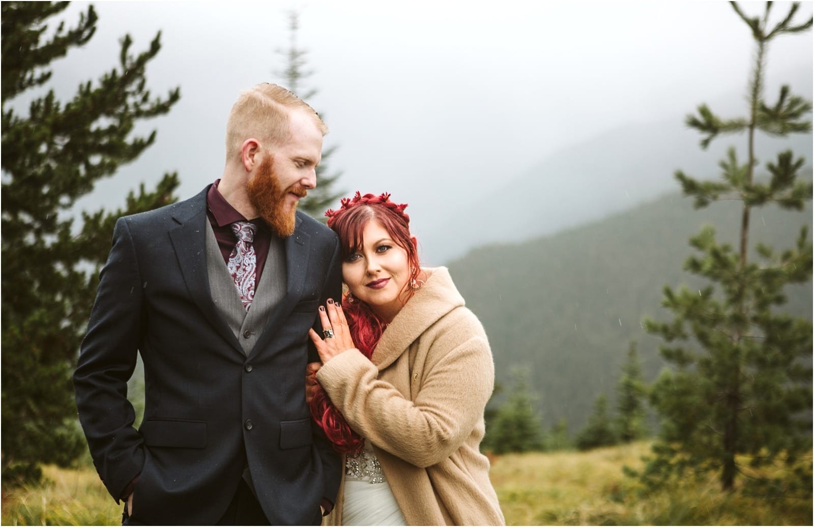 Premier Snohomish & Seattle Wedding Photographer | GSquared Weddings Photography A couple poses outdoors in front of misty mountains and pine trees for their Snohomish engagement. The man wears a dark suit and tie, while the woman, with red hair and a flower crown, smiles as she rests her head on his shoulder.                                   | Serving Snohomish, Seattle ,                  & Beyond