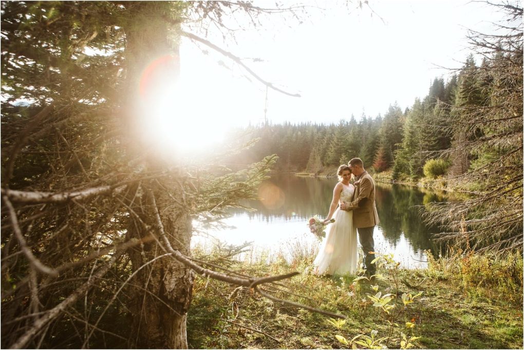 Premier snohomish & seattle wedding photographer | gsquared weddings photography a couple in wedding attire stands close together by a forested lake near snohomish surrounded by trees and sunlight streaming through the branches creating a serene and romantic seattle wedding atmosphere | serving snohomish seattle                   & beyond