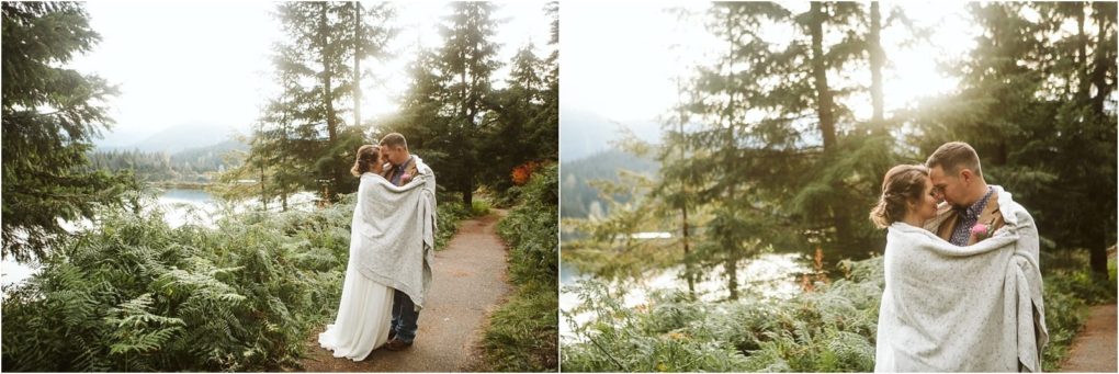 Premier snohomish & seattle wedding photographer | gsquared weddings photography a couple wrapped in a blanket embraces on a forested trail beside a lake sunlight streaming through tall trees and mountainscapturing the perfect snohomish seattle wedding engagement moment | serving snohomish seattle                   & beyond
