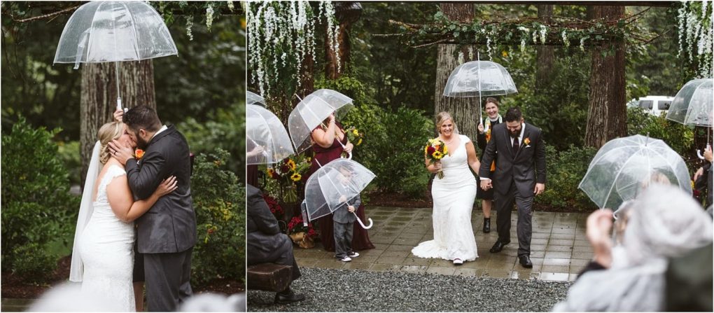 Premier snohomish & seattle wedding photographer | gsquared weddings photography a bride and groom kiss under a clear umbrella in the rain at their snohomish seattle wedding then walk hand in hand down an outdoor aisle as smiling guests with umbrellas look on amid lush trees and flowers | serving snohomish seattle                   & beyond