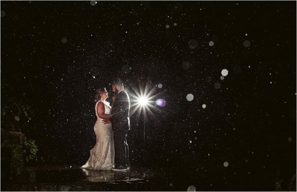Premier snohomish & seattle wedding photographer | gsquared weddings photography a bride and groom stand close together outdoors at night in the rain near snohomish dramatically illuminated from behind creating a romantic and dreamy seattle wedding atmosphere with sparkling raindrops all around them | serving snohomish seattle                   & beyond