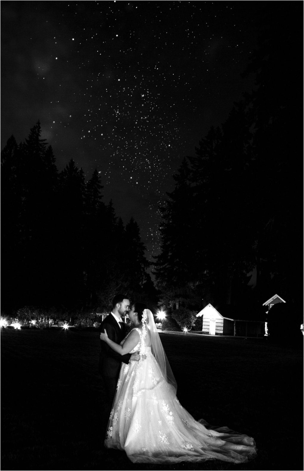 Premier snohomish & seattle wedding photographer | gsquared weddings photography a bride and groom embrace outdoors at night beneath a star filled sky surrounded by trees and softly lit buildings in the background This romantic black and white photo captures a magical snohomish seattle wedding moment | serving snohomish seattle                   & beyond