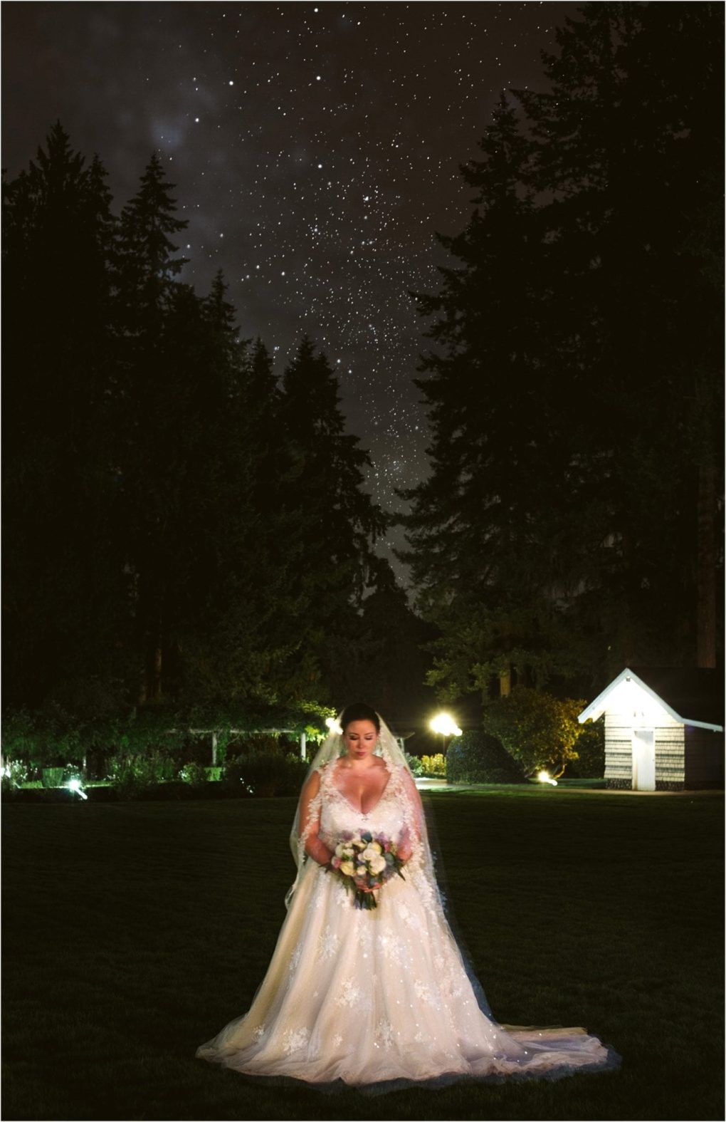 Premier snohomish & seattle wedding photographer | gsquared weddings photography a bride in a white wedding gown stands on a grassy lawn at night holding a bouquet She is illuminated while surrounded by trees under a star filled sky at a snohomish seattle wedding with a small white structure behind her | serving snohomish seattle                   & beyond