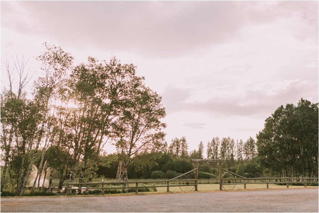 Premier snohomish & seattle wedding photographer | gsquared weddings photography a rustic wooden gate with wagon wheels stands at the entrance to a scenic field near snohomish perfect for a seattle wedding or engagement Tall trees border the sunset sky with a windmill and pond visible in the soft cloudy background | serving snohomish seattle                   & beyond
