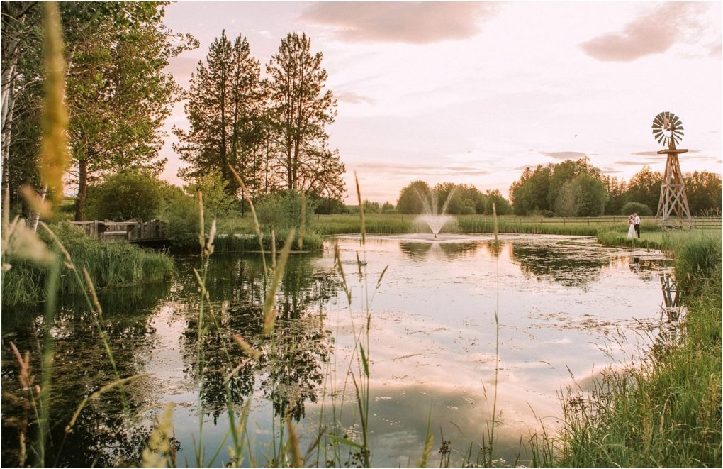 Premier snohomish & seattle wedding photographer | gsquared weddings photography a serene pond at sunset reflects trees and a cloudy sky with a windmill fountain and a person by the waters edge Tall grasses frame this peaceful snohomish sceneperfect for a seattle wedding or engagement backdrop | serving snohomish seattle                   & beyond