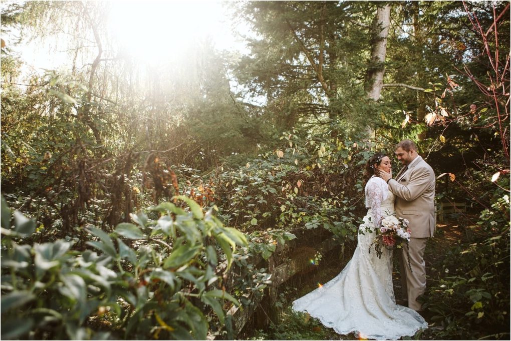 Premier snohomish & seattle wedding photographer | gsquared weddings photography a bride and groom stand close together in a lush sunlit snohomish forest The bride holds a bouquet and wears a white dress while the groom wears a tan suitsunlight glowing through the trees creates a romantic seattle wedding atmosphere | serving snohomish seattle                   & beyond