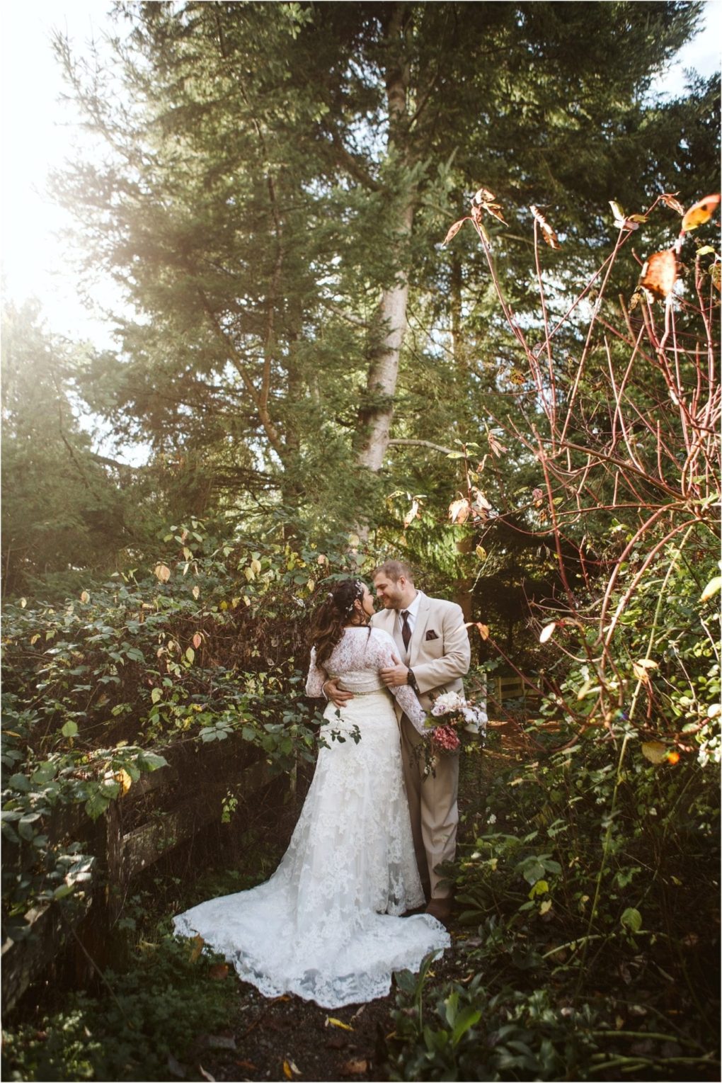 Premier snohomish & seattle wedding photographer | gsquared weddings photography a bride and groom stand embracing on a forest path near snohomish surrounded by lush greenery and sunlight filtering through tall trees The bride wears a white lace gown and the groom is in a light suit both looking happy and in love | serving snohomish seattle                   & beyond