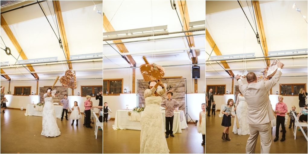 Premier snohomish & seattle wedding photographer | gsquared weddings photography at a snohomish wedding a bride and groom take turns swinging a large wooden paddle at a giant heart shaped piñata indoors while guests including children watch and cheer in the beautifully decorated hall | serving snohomish seattle                   & beyond