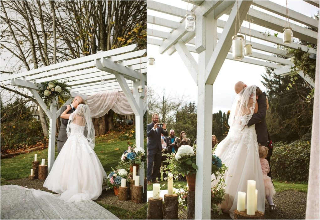 Premier snohomish & seattle wedding photographer | gsquared weddings photography a snohomish bride and groom share a kiss under a white pergola decorated with flowers and draped fabric at their outdoor wedding surrounded by candles and trees as guests from seattle watch and celebrate their special engagement | serving snohomish seattle                   & beyond