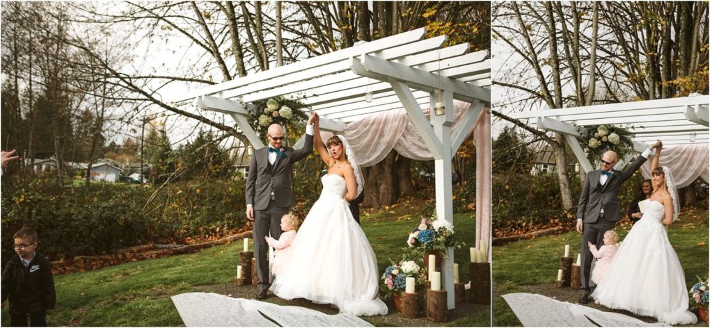 Premier snohomish & seattle wedding photographer | gsquared weddings photography a bride and groom stand under a white pergola decorated with flowers and drapery during their snohomish wedding The bride lifts her arm joyfully while a young child holds her gown and a boy stands off to the left in the grassy outdoor setting | serving snohomish seattle                   & beyond