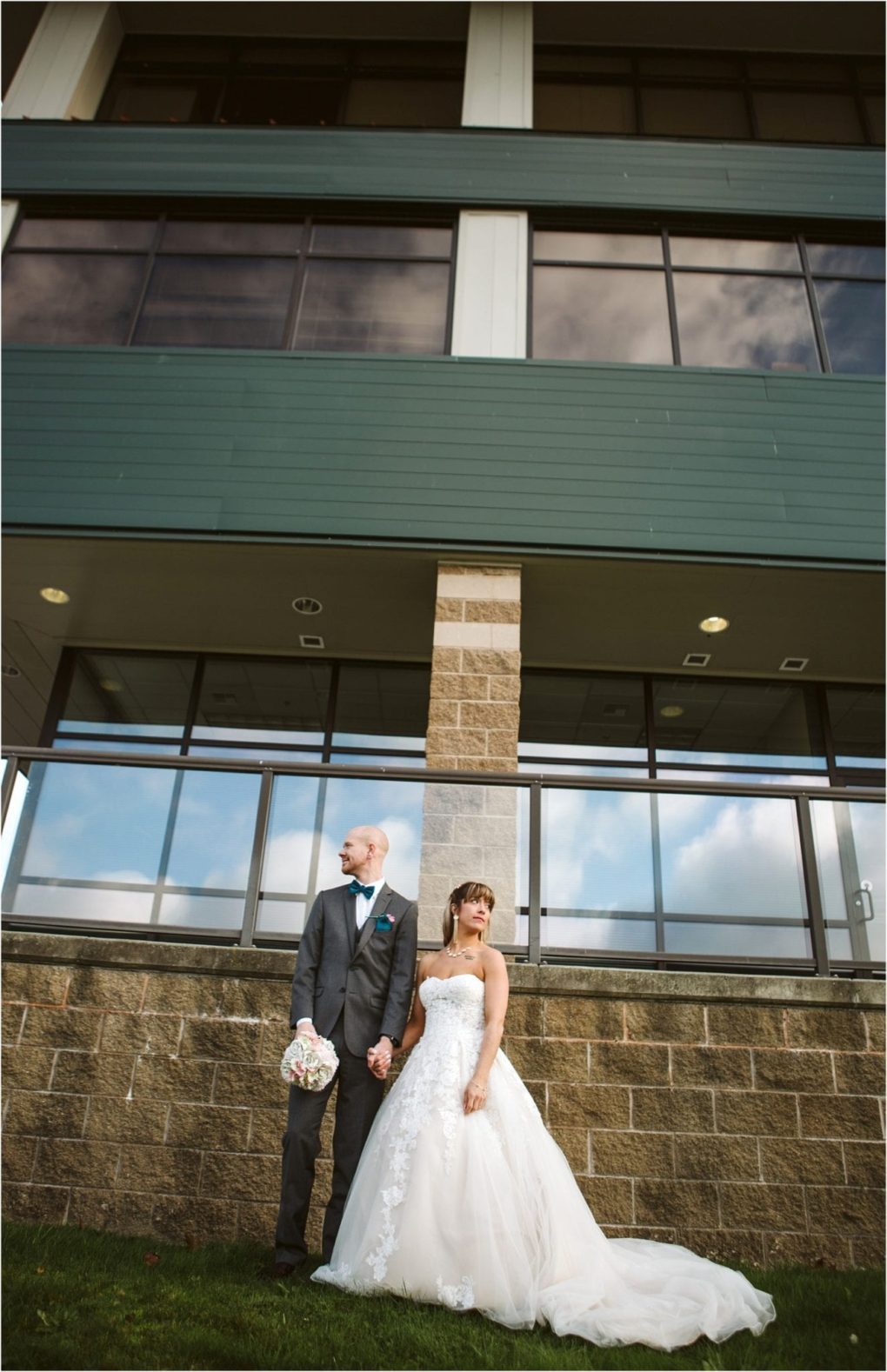 Premier snohomish & seattle wedding photographer | gsquared weddings photography a bride in a white dress and a groom in a gray suit stand holding hands outside a modern building during their snohomish seattle wedding both looking away from each other The bride holds a bouquet and wears a strapless lace gown | serving snohomish seattle                   & beyond