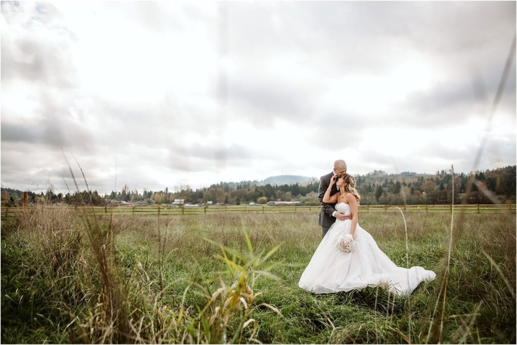 Premier snohomish & seattle wedding photographer | gsquared weddings photography a bride in a white dress and groom in a suit embrace in a grassy field under a cloudy sky with trees and distant hills behind themthe perfect snohomish seattle wedding engagement backdrop | serving snohomish seattle                   & beyond