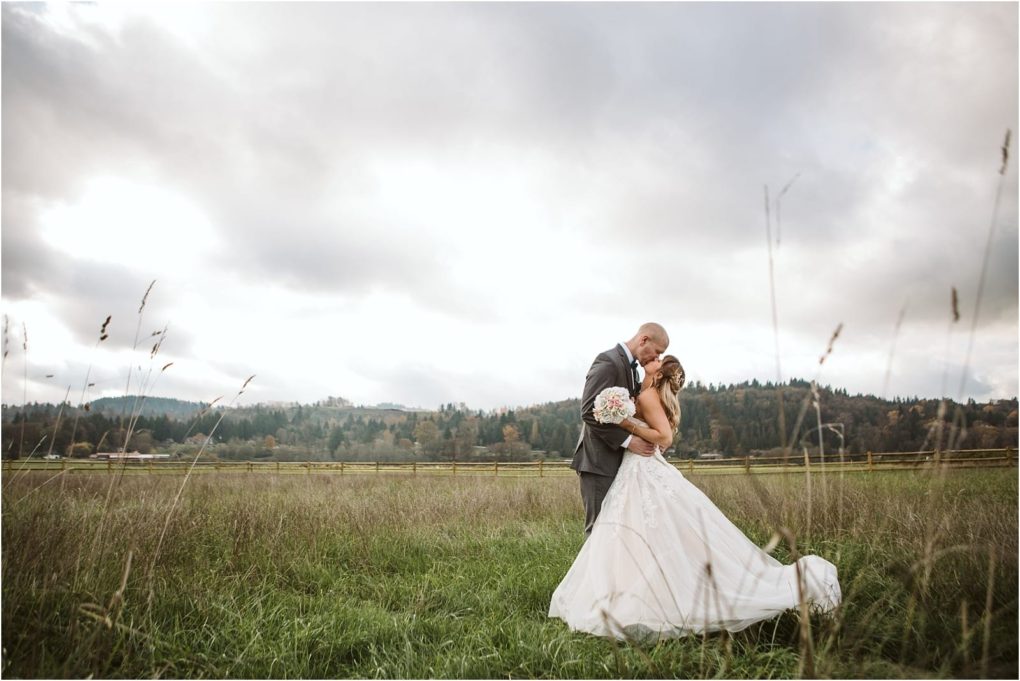 Premier snohomish & seattle wedding photographer | gsquared weddings photography a bride and groom embrace in a grassy snohomish field under a cloudy sky with rolling hills and trees beyond The groom holds a bouquet as they smile at each other dressed in formal wedding attire for their seattle wedding engagement | serving snohomish seattle                   & beyond
