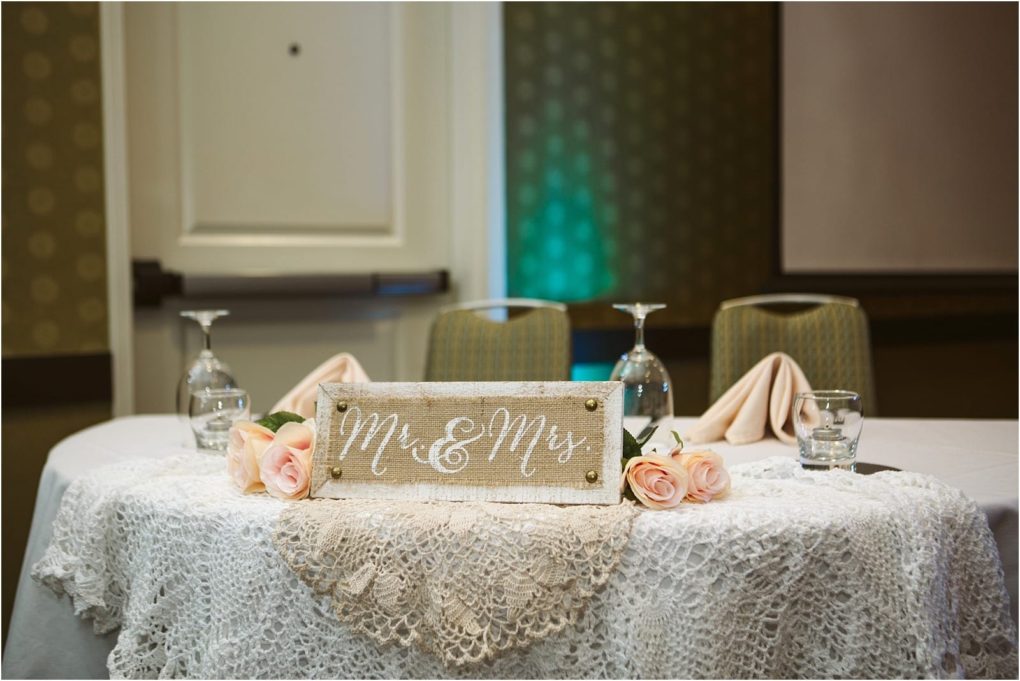 Premier snohomish & seattle wedding photographer | gsquared weddings photography a round table with a lace tablecloth displays a mr & mrs Sign pink roses glassware and folded napkins set up for a snohomish wedding reception Three chairs are in the background | serving snohomish seattle                   & beyond