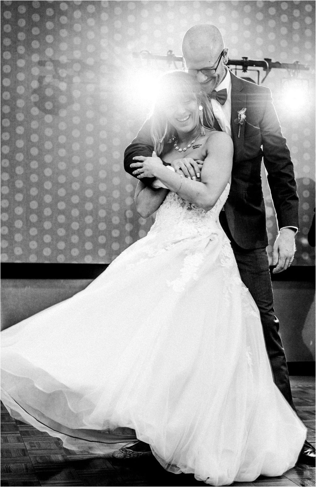 Premier snohomish & seattle wedding photographer | gsquared weddings photography a joyful bride in a flowing wedding dress twirls on the dance floor while being embraced from behind by her smiling groom in a suit during their snohomish seattle wedding both lit dramatically by bright lights in the background | serving snohomish seattle                   & beyond