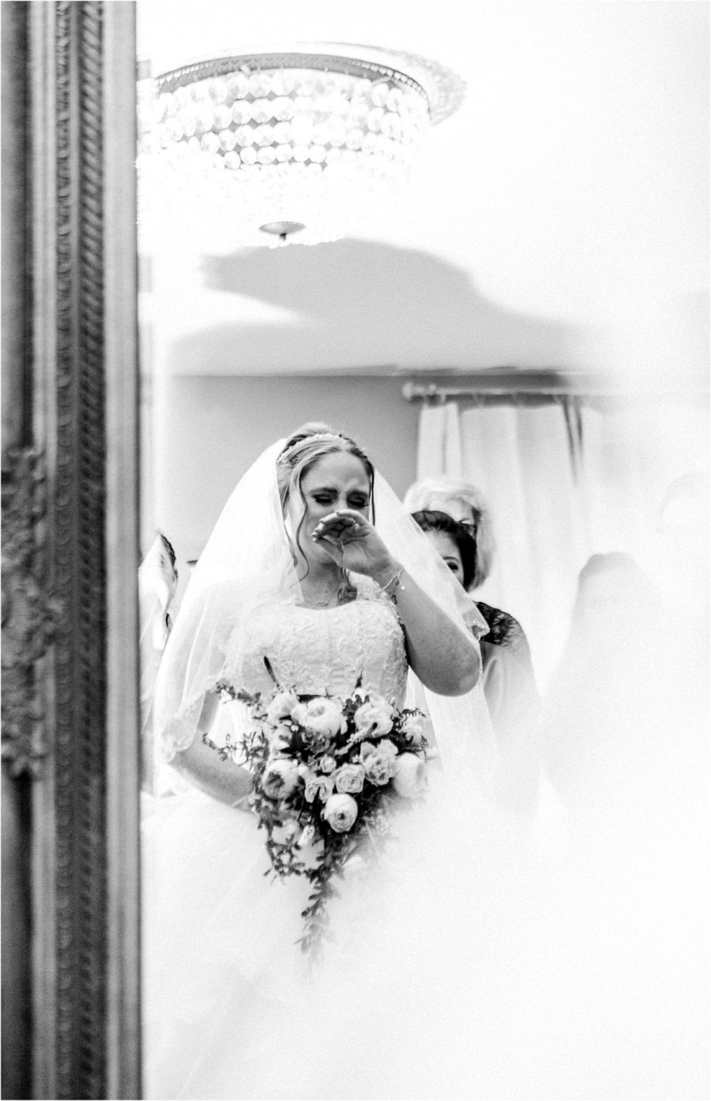 Premier snohomish & seattle wedding photographer | gsquared weddings photography a bride in a wedding dress and veil wipes away a tear while holding a bouquet standing indoors under soft lighting and a chandelier This snohomish seattle wedding image has a dreamy ethereal quality | serving snohomish seattle                   & beyond