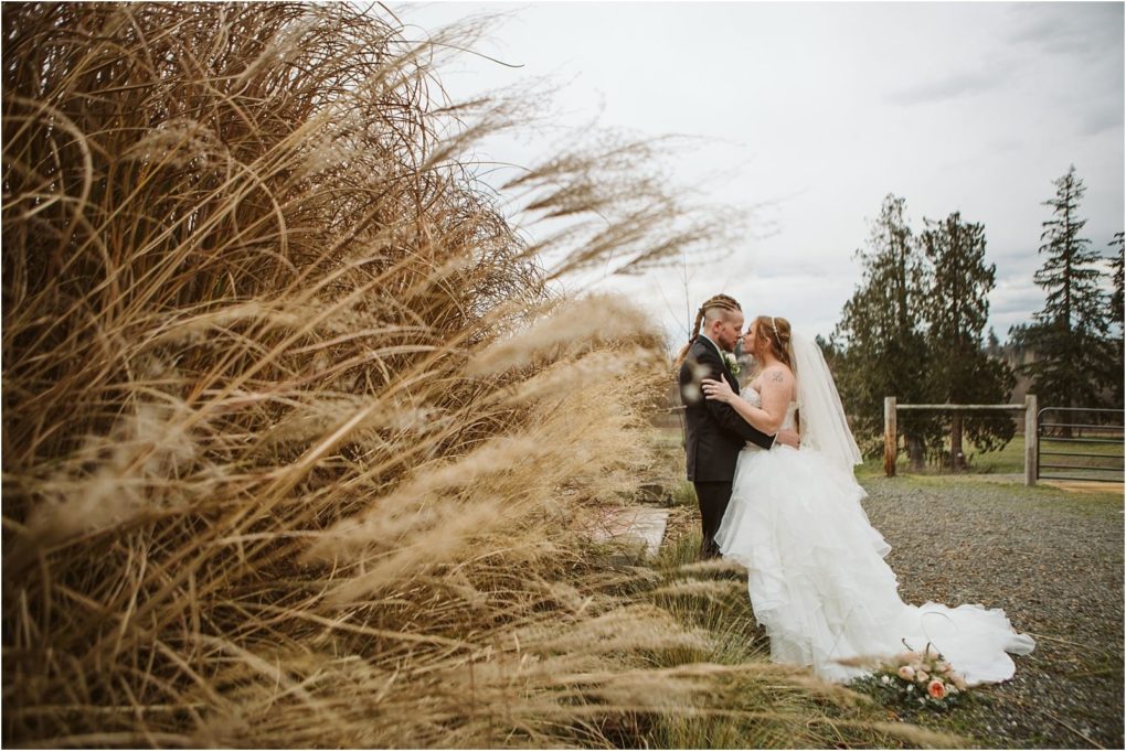 Premier snohomish & seattle wedding photographer | gsquared weddings photography a bride and groom embrace outdoors beside tall golden grass at their snohomish wedding with a bouquet on the ground nearby The overcast sky distant trees and a wooden fence set a serene seattle engagement scene | serving snohomish seattle                   & beyond