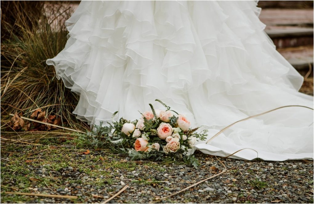 Premier snohomish & seattle wedding photographer | gsquared weddings photography a white ruffled wedding dress trails on gravel beside grass with a bouquet of pale pink and white flowers lying on the groundcapturing the elegance of a snohomish or seattle wedding | serving snohomish seattle                   & beyond