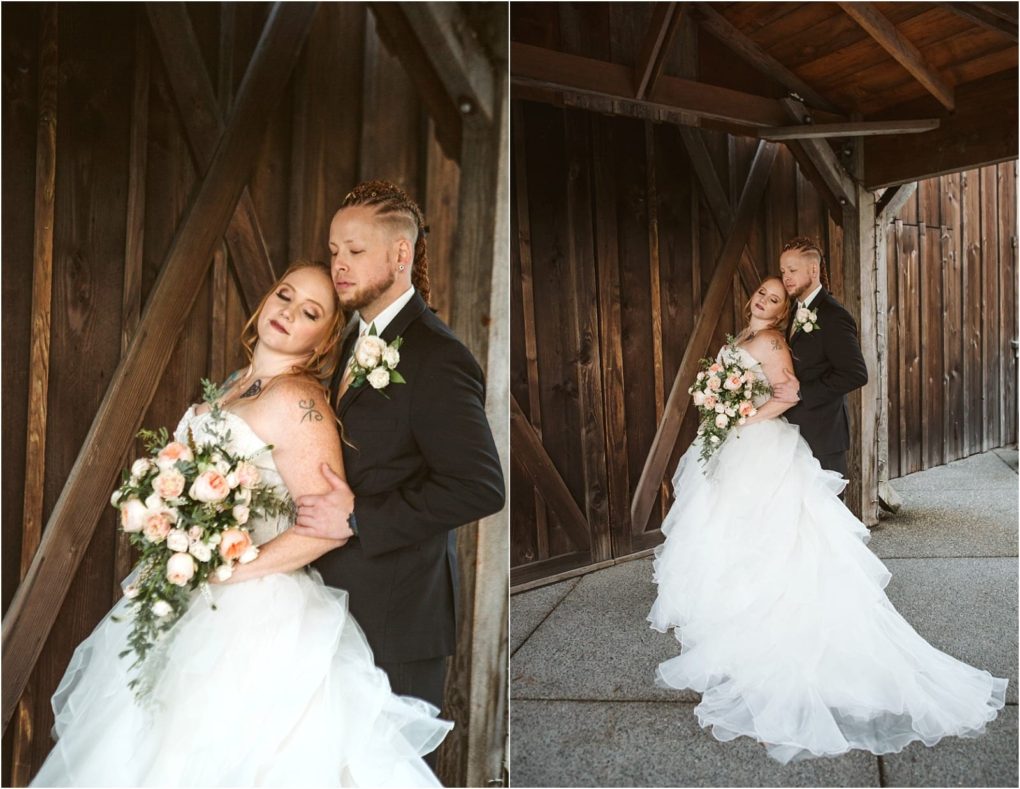 Premier snohomish & seattle wedding photographer | gsquared weddings photography a bride in a white gown and a groom in a black suit embrace closely posing in front of a rustic wooden wall at their snohomish seattle wedding The bride holds a bouquet of pale pink flowers as they look serene and content | serving snohomish seattle                   & beyond