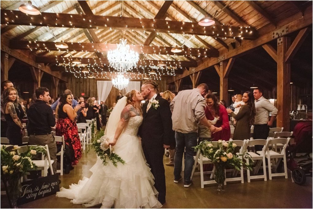 Premier snohomish & seattle wedding photographer | gsquared weddings photography a bride and groom kiss in the aisle of a rustic warmly lit snohomish barn decorated with chandeliers and string lights surrounded by seated wedding guests and lush floral arrangements capturing a magical seattle wedding moment | serving snohomish seattle                   & beyond