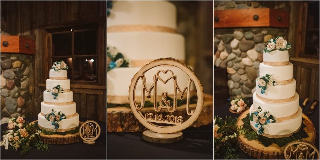 Premier snohomish & seattle wedding photographer | gsquared weddings photography a four tiered white wedding cake with gold accents and floral decorations sits on a wooden stand next to a round wooden sign engraved with m&m 12 14 2018 in a rustic snohomish seattle wedding setting with stone and wood walls | serving snohomish seattle                   & beyond