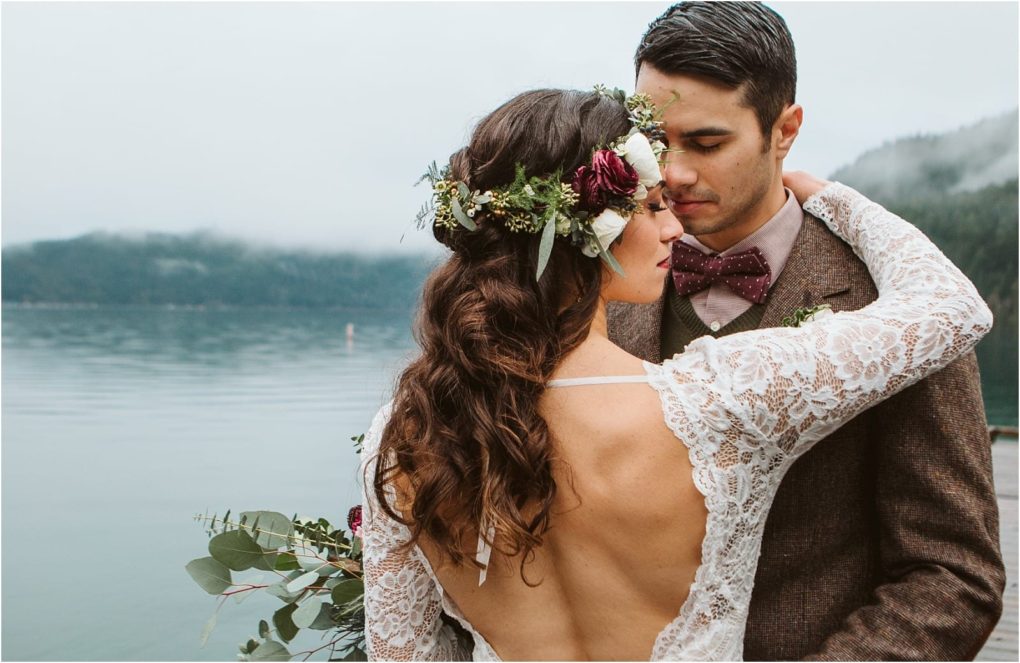 Premier snohomish & seattle wedding photographer | gsquared weddings photography a bride in a lace dress with floral crown embraces her groom in a brown suit and bow tie by a serene lake surrounded by misty mountainscapturing the magic of a snohomish seattle wedding engagement | serving snohomish seattle                   & beyond
