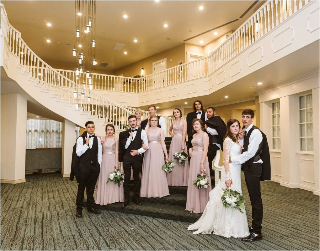 Premier snohomish & seattle wedding photographer | gsquared weddings photography a snohomish wedding party poses indoors bridesmaids in matching mauve dresses and groomsmen in black suits stand around the bride and groom under elegant lighting and a sweeping staircase capturing a classic seattle engagement vibe | serving snohomish seattle                   & beyond