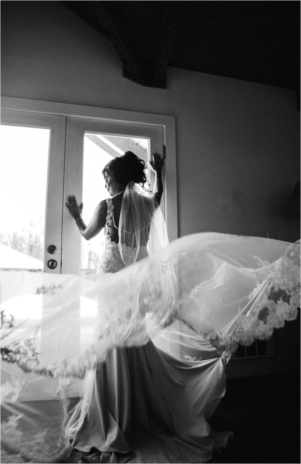 Premier snohomish & seattle wedding photographer | gsquared weddings photography black and white photo of a bride in a flowing gown and veil standing by a glass door looking outside with one hand on the doorperfect inspiration for your snohomish or seattle wedding engagement Her veil sweeps dramatically through the air | serving snohomish seattle                   & beyond