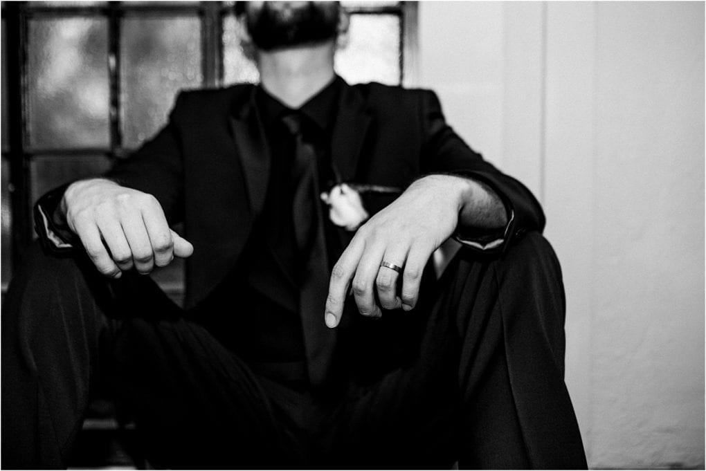 Premier snohomish & seattle wedding photographer | gsquared weddings photography a man in a black suit and tie sits with his knees up hands resting on his knees wearing a ring and boutonnièrecaptured at a snohomish seattle wedding His face is out of focus in this black and white image | serving snohomish seattle                   & beyond