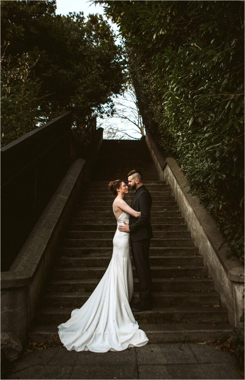 Premier snohomish & seattle wedding photographer | gsquared weddings photography a bride in a white gown and a groom in a black suit embrace on a stone staircase outdoors surrounded by lush green foliage capturing the romance of a snohomish seattle wedding engagement | serving snohomish seattle                   & beyond