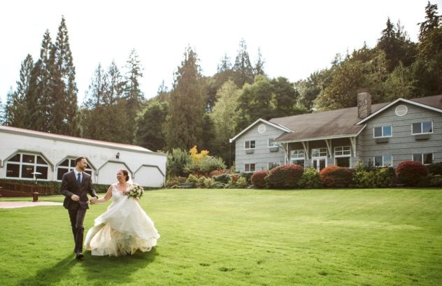 Premier snohomish & seattle wedding photographer | gsquared weddings photography a bride and groom run hand-in-hand across a green lawn smiling joyfully Their wedding photographer captures the moment with a grey house barn-style building and tall trees providing a lush backdrop to these timeless photos | candid wedding photo by gsquared weddings Washington wedding venue carnation farms