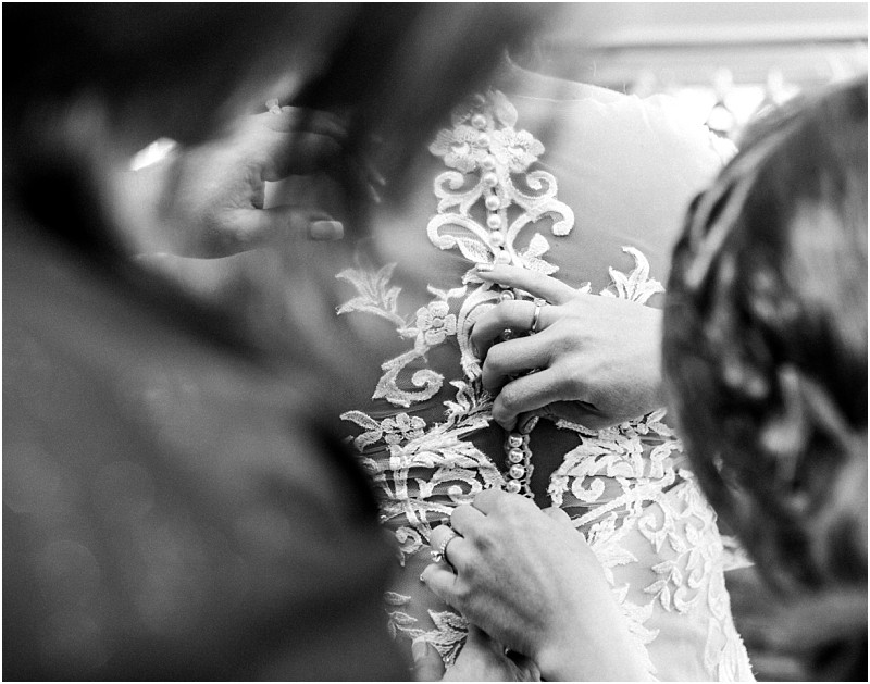 Premier snohomish & seattle wedding photographer | gsquared weddings photography close up in black and white of hands fastening intricate buttons on the back of a lace wedding dress with blurred figures assisting from both sidesa timeless moment from a snohomish seattle wedding engagement | serving snohomish seattle                   & beyond
