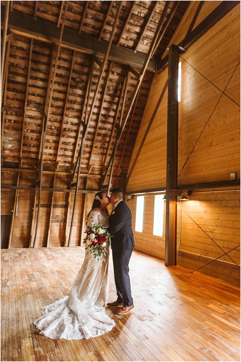 Premier snohomish & seattle wedding photographer | gsquared weddings photography a bride and groom share a kiss in the center of a rustic wooden barn with high vaulted ceilings and exposed beams Sunlight streams in through tall windows illuminating the couple during their snohomish seattle wedding | serving snohomish seattle                   & beyond