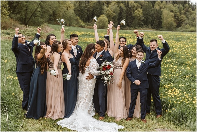 Premier snohomish & seattle wedding photographer | gsquared weddings photography a bride and groom kiss in the center of their snohomish wedding party standing outdoors in a field Bridesmaids in blush dresses and groomsmen in navy suits cheer raise flower bouquets and celebrate together | serving snohomish seattle                   & beyond