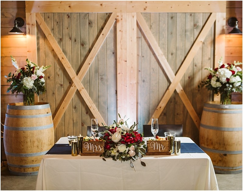 Premier snohomish & seattle wedding photographer | gsquared weddings photography a rustic snohomish wedding sweetheart table with mr  and mrs  signs red and white flower centerpiece gold candles and champagne glasses Wooden barn doors and two large floral arrangements on wine barrels complete this seattle engagement setting | serving snohomish seattle                   & beyond