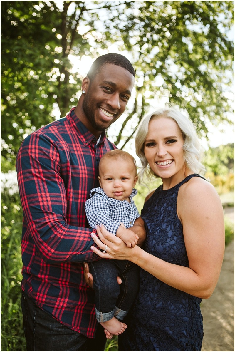 Premier snohomish & seattle wedding photographer | gsquared weddings photography a smiling couple stands outdoors holding their baby in matching blue checks Perfect for a snohomish or seattle wedding engagement shoot sunlight filters through green trees behind them The man wears red and navy plaid the woman wears a navy dress | serving snohomish seattle                   & beyond