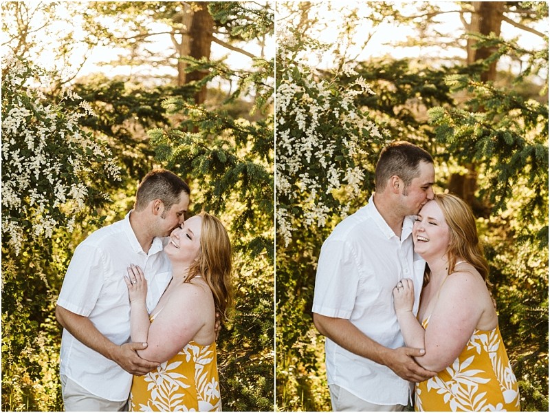 Premier snohomish & seattle wedding photographer | gsquared weddings photography a couple stands closely together outdoors among green trees and white flowers During their snohomish engagement the man in a white shirt kisses the smiling woman with red hair in a yellow patterned dress on the forehead and cheek | serving snohomish seattle                   & beyond