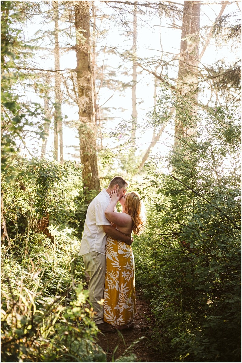 Premier snohomish & seattle wedding photographer | gsquared weddings photography a couple stands on a forest path near snohomish surrounded by greenery and sunlight embracing and sharing a kiss The woman wears a yellow floral dress and the man wears a white shirt and beige pantscapturing a perfect seattle engagement moment | serving snohomish seattle                   & beyond
