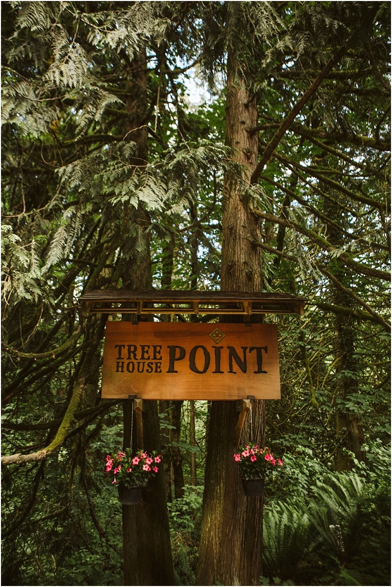 Premier snohomish & seattle wedding photographer | gsquared weddings photography a wooden sign reading tree house point hangs between two trees in a lush forest near snohomish perfect for a seattle wedding or engagement Two small flower baskets with pink flowers are attached to the bottom of the sign | serving snohomish seattle                   & beyond