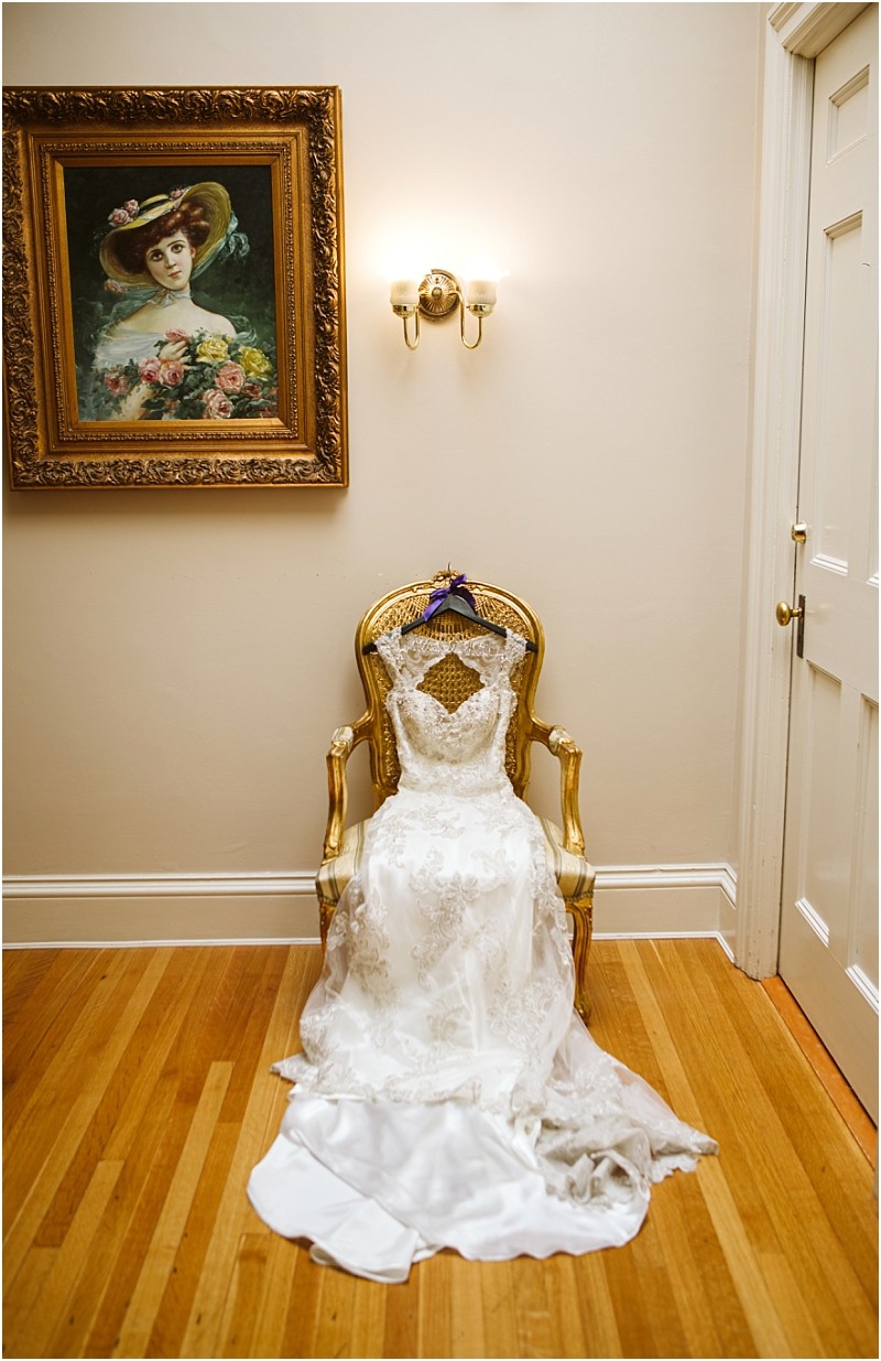 Premier snohomish & seattle wedding photographer | gsquared weddings photography a white lace wedding dress draped over an ornate gold chair sits beneath a wall sconce in a hallway perfect for a snohomish or seattle wedding with a framed painting of a woman in a hat hanging above | serving snohomish seattle                   & beyond